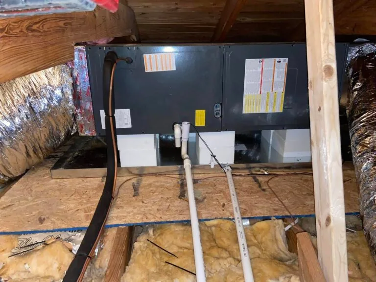 Attic air handler unit with PVC condensate drain lines and wiring on plywood platform, West Monroe