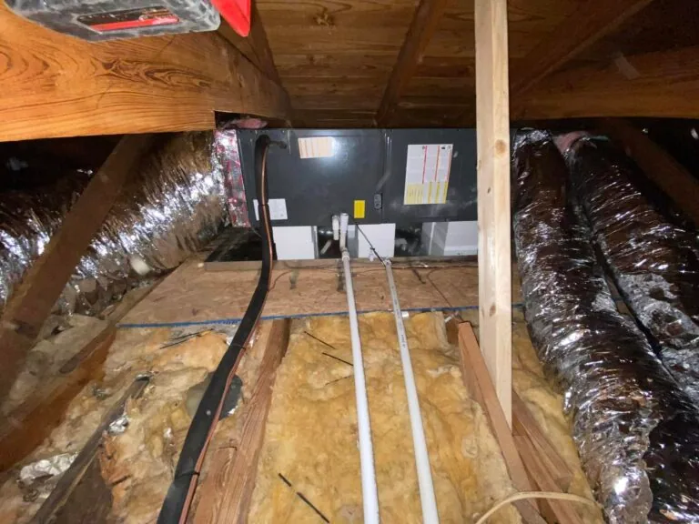 Attic HVAC air handler unit flanked by insulated flex ducts with PVC condensate lines running through insulation