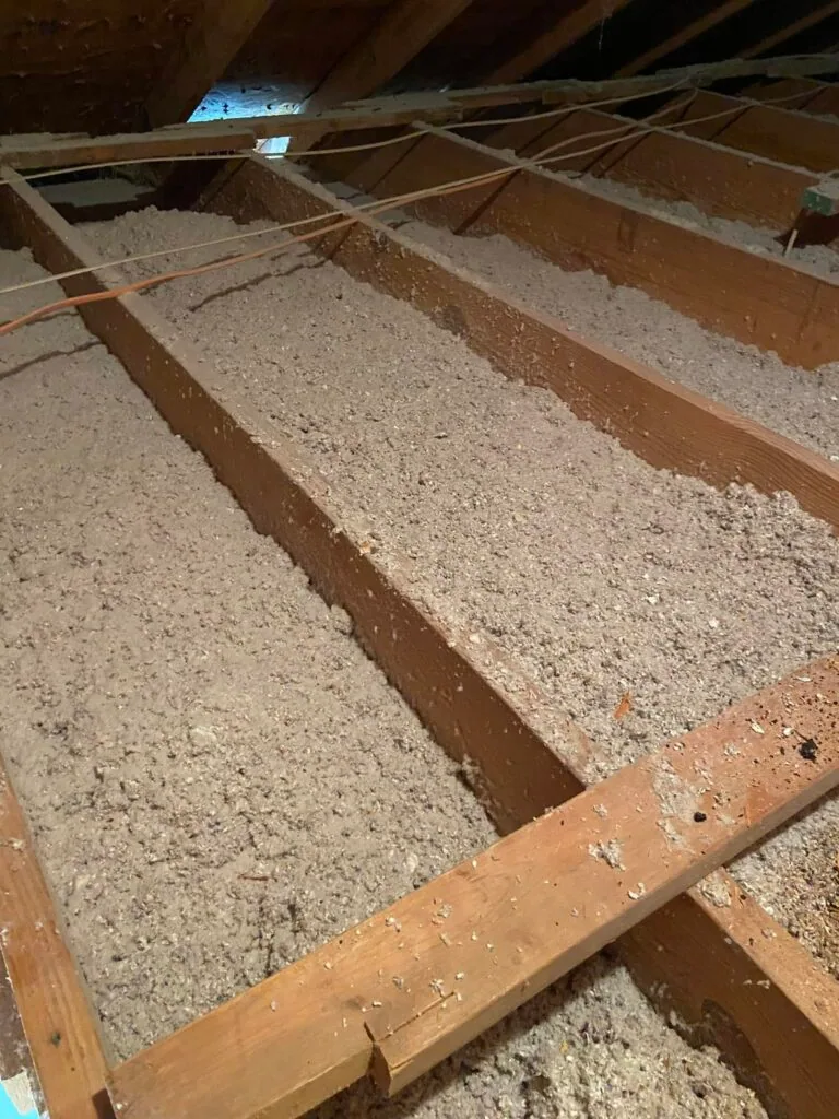 Attic space with wood joists filled with blown-in insulation and electrical wiring visible, West Monroe home