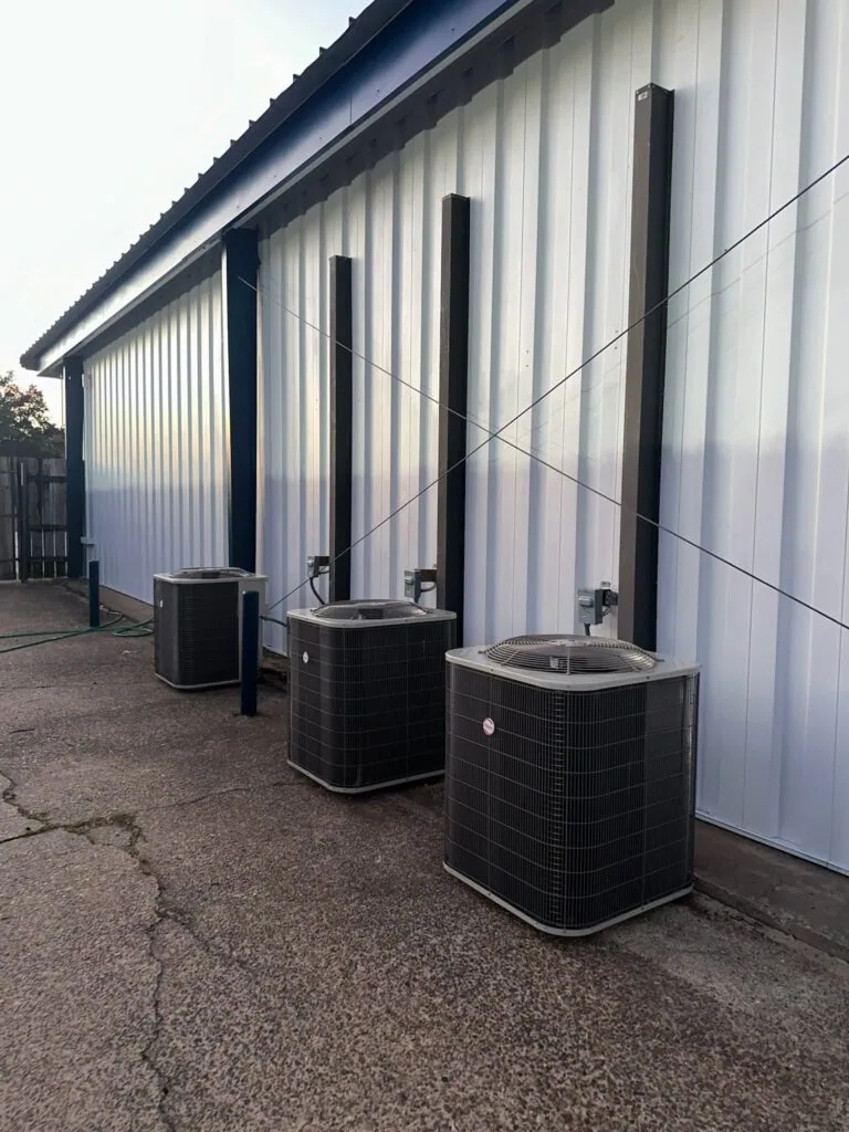 Three outdoor HVAC condenser units lined up along the exterior wall of a metal commercial building