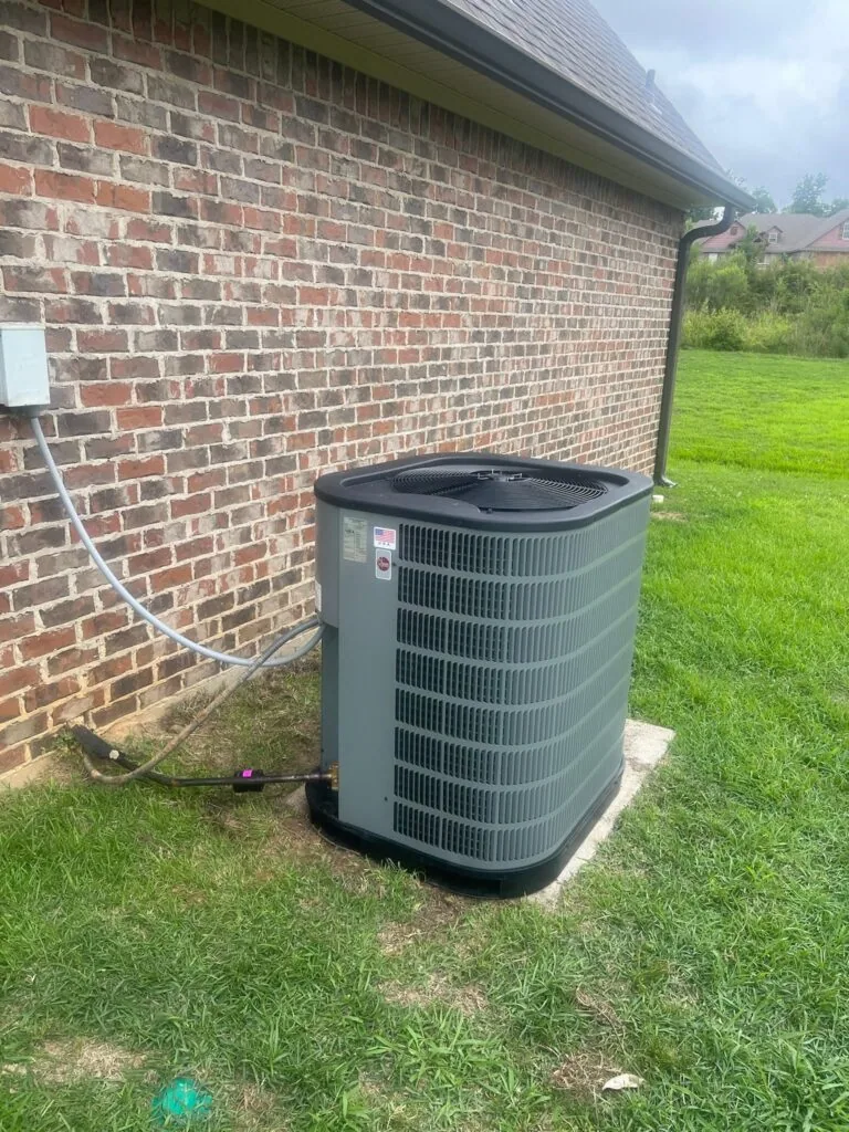 Outdoor air conditioning condenser unit on concrete pad beside a brick house with refrigerant lines running to the wall
