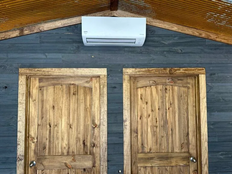 White Daikin ductless mini-split indoor unit mounted high on a wood gable wall between two rustic wooden doors