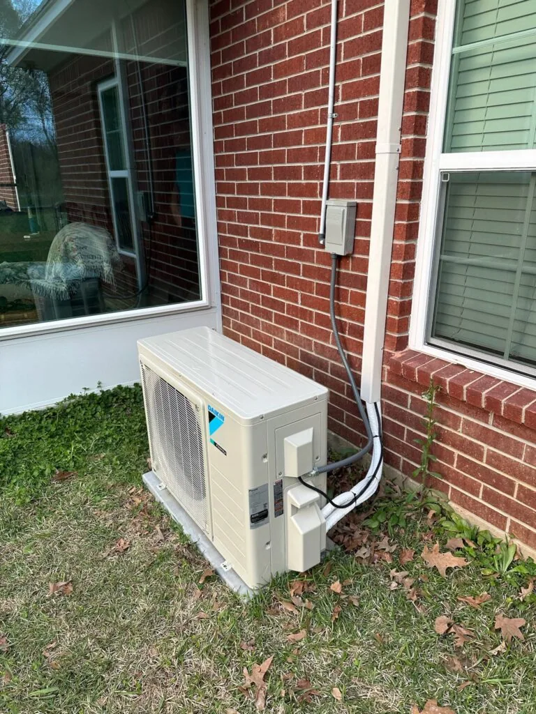 Daikin ductless heat pump condenser unit mounted outside a brick home near a sunroom window in West Monroe, LA
