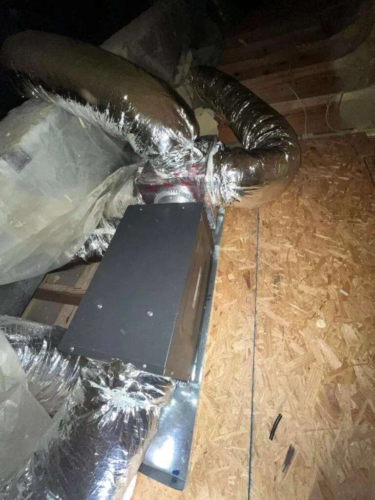 Flexible insulated ductwork connected to a metal junction box on plywood decking in an attic