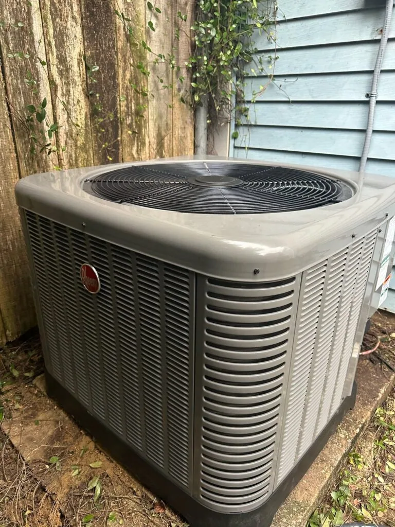 Rheem outdoor condenser unit on concrete pad next to a wood fence and house siding