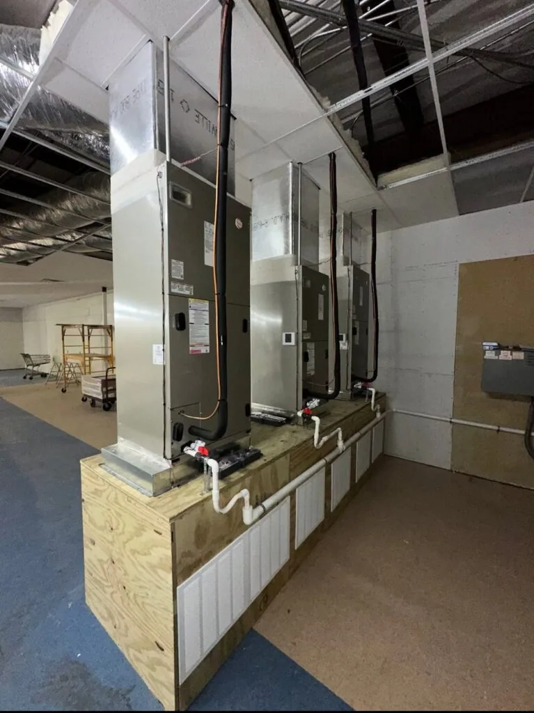 Three vertical air handler units mounted on a wood platform in a commercial building ceiling space in West Monroe