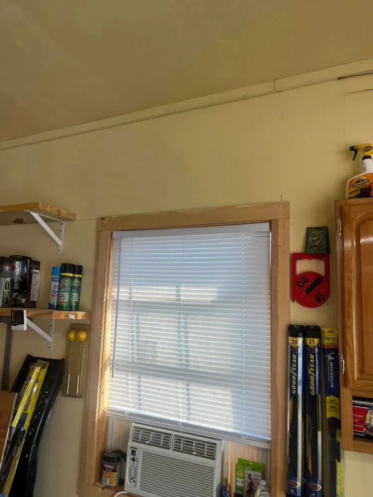 Small window air conditioning unit mounted in a wood-framed window inside a garage or shop