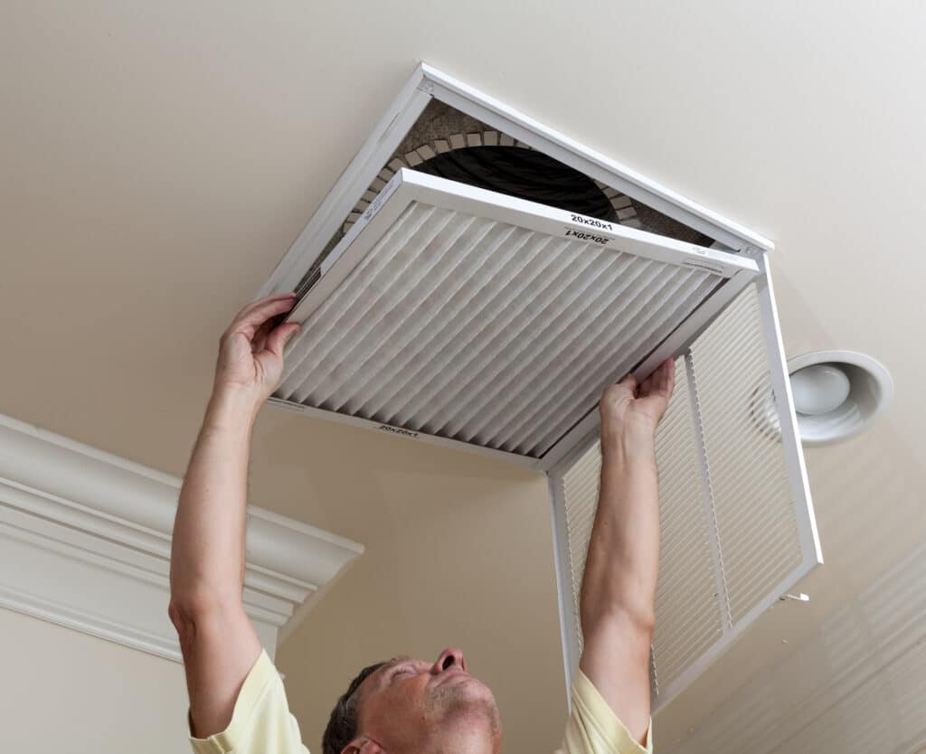 Older man reaching up to open a ceiling return grille and access the air filter