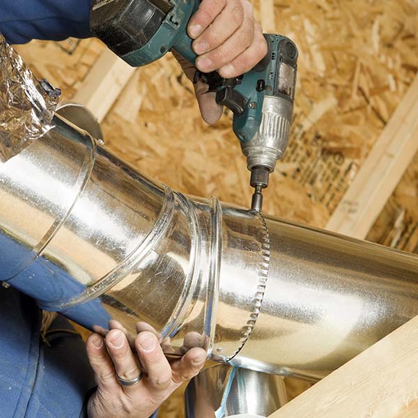 Worker driving a screw into a round galvanized duct joint with a cordless impact driver