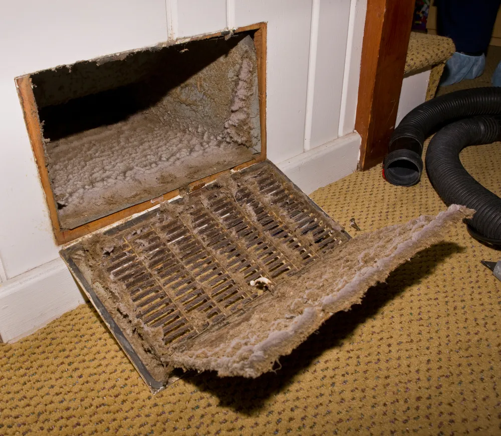 Return air grille pulled open to reveal a thick mat of dust and debris inside the vent