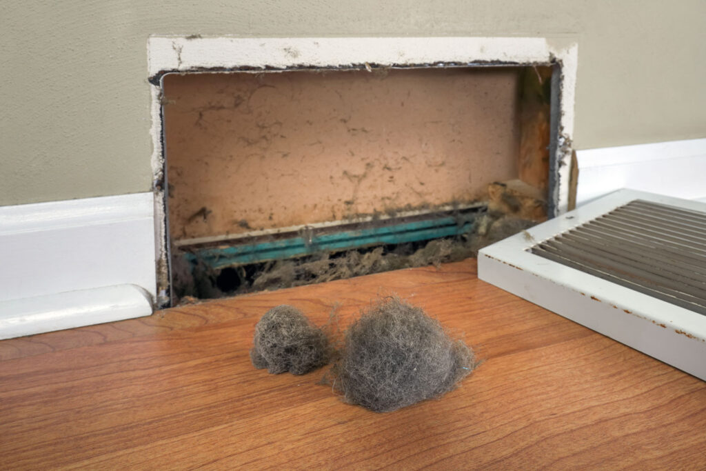 Clumps of gray dust pulled from an open baseboard vent, with the grille set on the floor