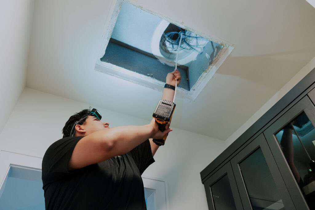 Technician feeding a cleaning whip tool into an open ceiling return vent