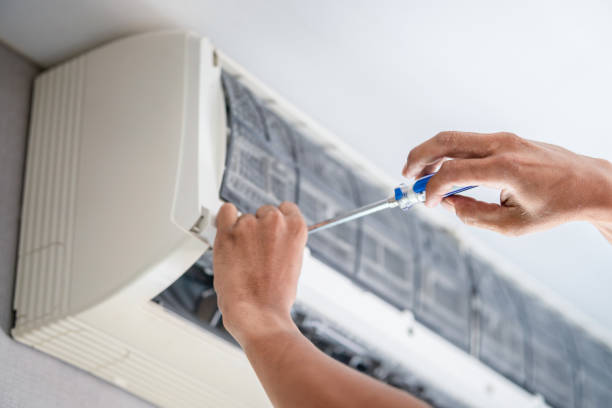 Technician using a screwdriver on an open wall-mounted ductless air conditioner indoor unit