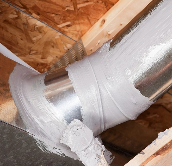 Metal duct joints coated with white mastic sealant in an attic between wood rafters