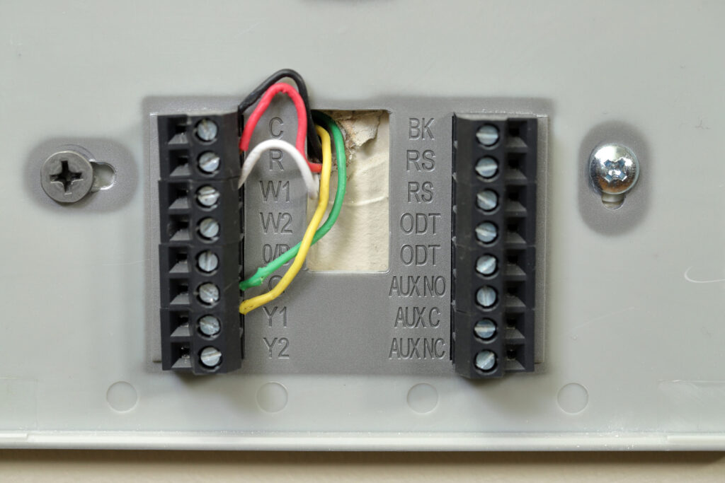 Close-up of a thermostat wall plate with red, white, green, and yellow wires in labeled terminals