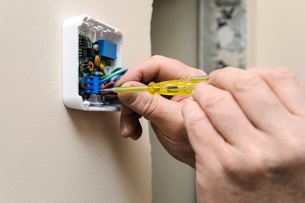 Hands using a yellow screwdriver to wire the circuit board of a wall thermostat