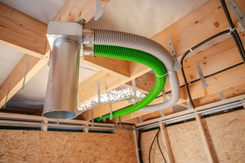 Green and gray flexible ventilation hoses connected to a metal duct box in open wood framing