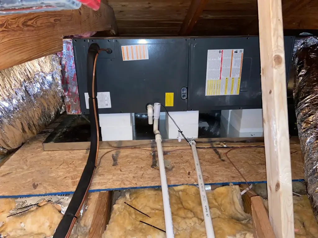 HVAC air handler unit installed in a home attic with insulated ductwork and PVC drain lines