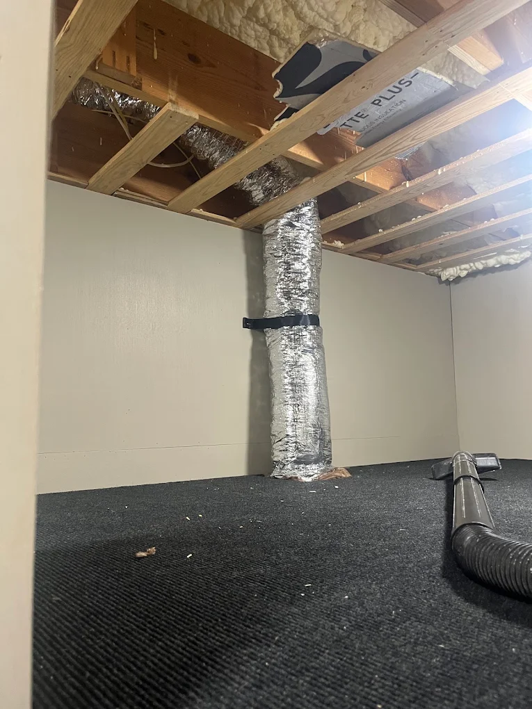 Insulated flex duct running vertically from floor joists into a crawlspace, secured with a strap